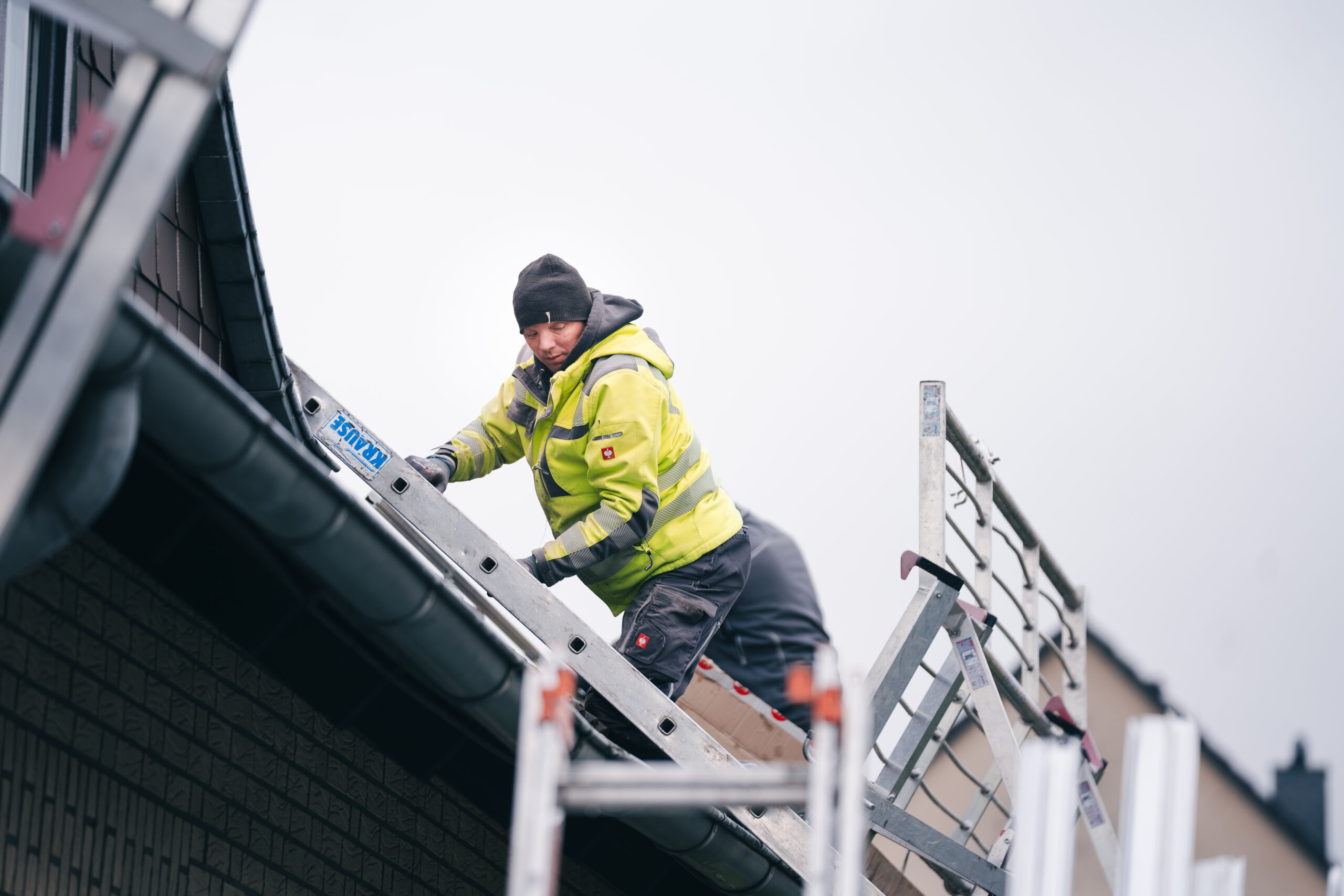 Mitarbeiter der MMS GmbH in Warnkleidung arbeitet auf einer Leiter an der Vorbereitung einer Photovoltaikanlage am Hausdach.