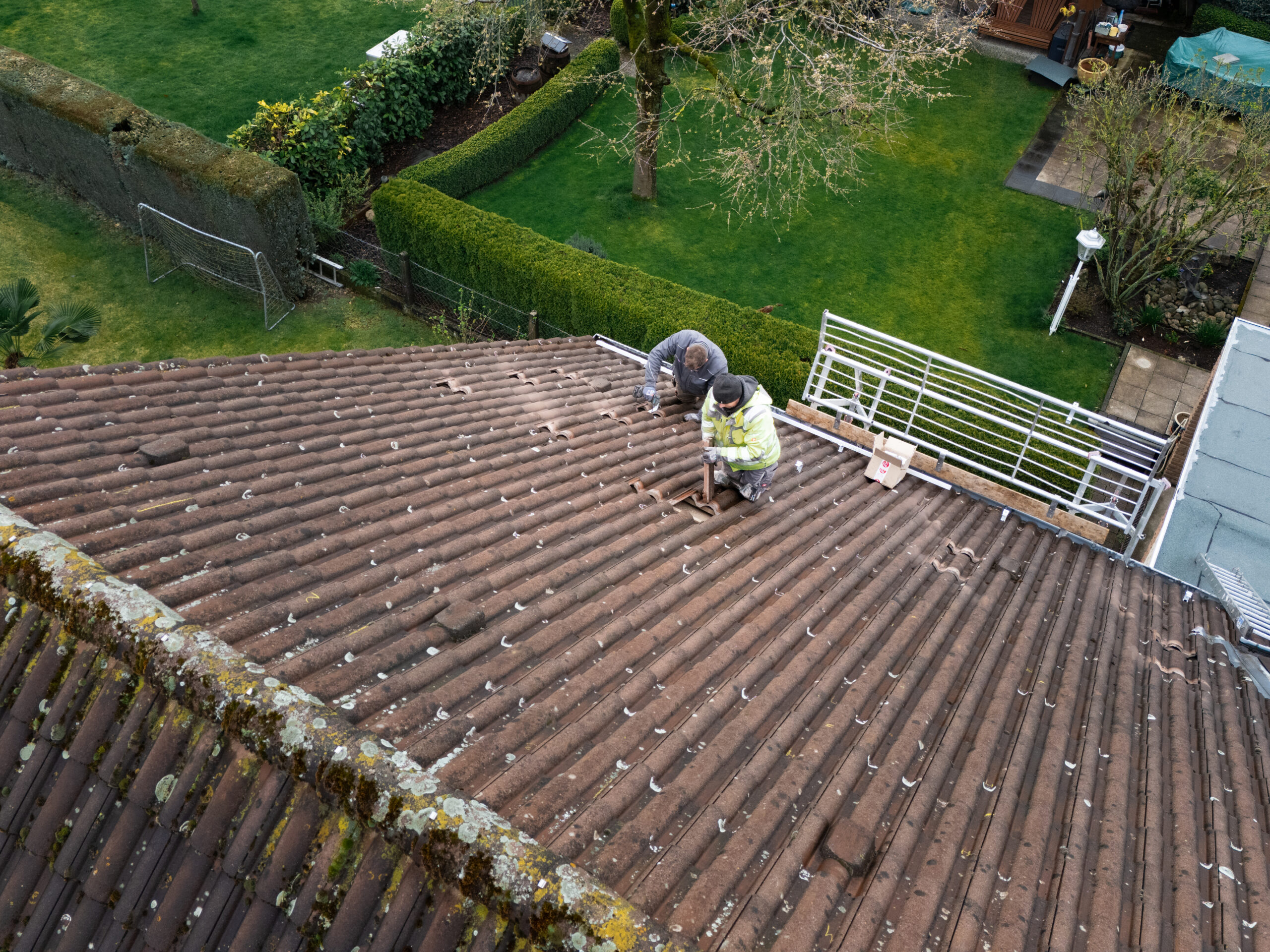 Zwei Mitarbeiter der MMS GmbH bereiten ein Hausdach für die Installation einer Photovoltaikanlage vor und befestigen Montagesysteme.