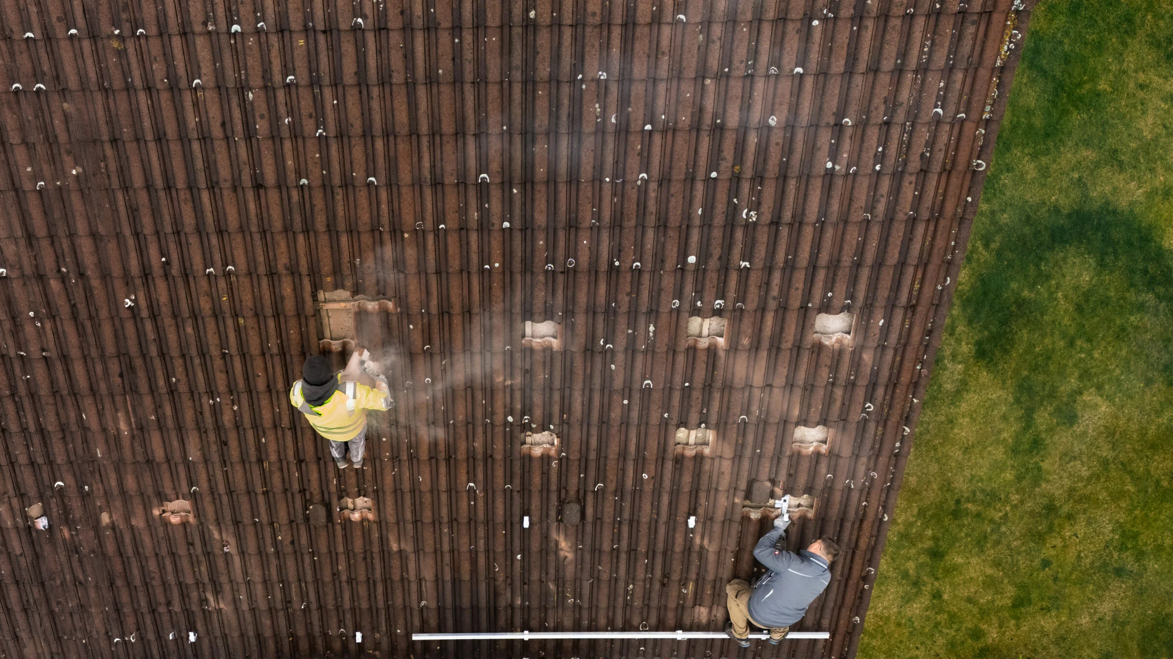 Zwei Mitarbeiter der MMS GmbH arbeiten auf einem Hausdach und bereiten die Montage einer Photovoltaikanlage vor, aufgenommen aus der Vogelperspektive.